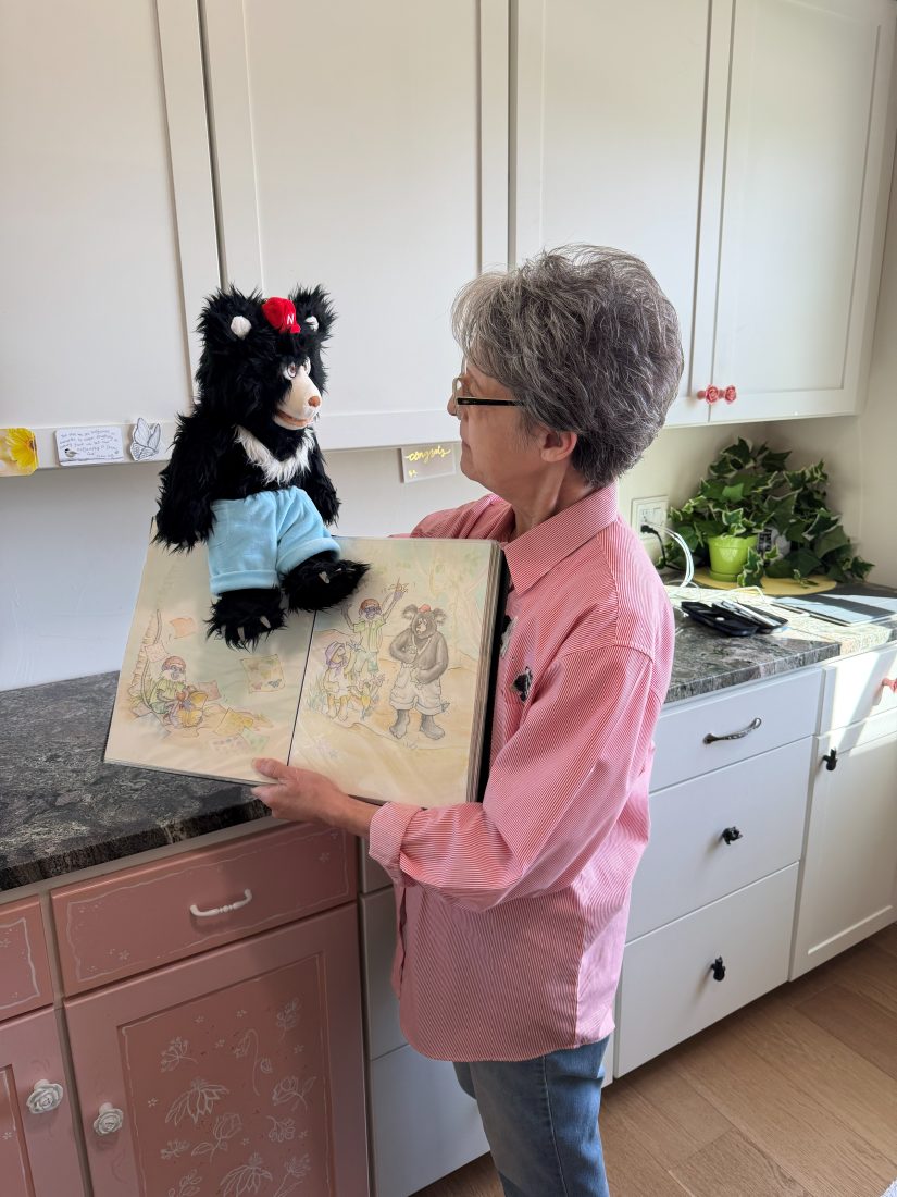 Alora holding open a book of illustrations with the Nawful puppet perched on top