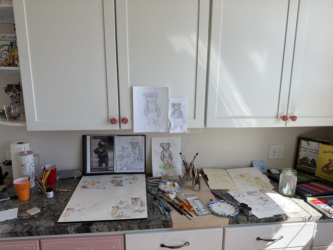 Character sketches taped to white cabinets above a counter full of art supplies